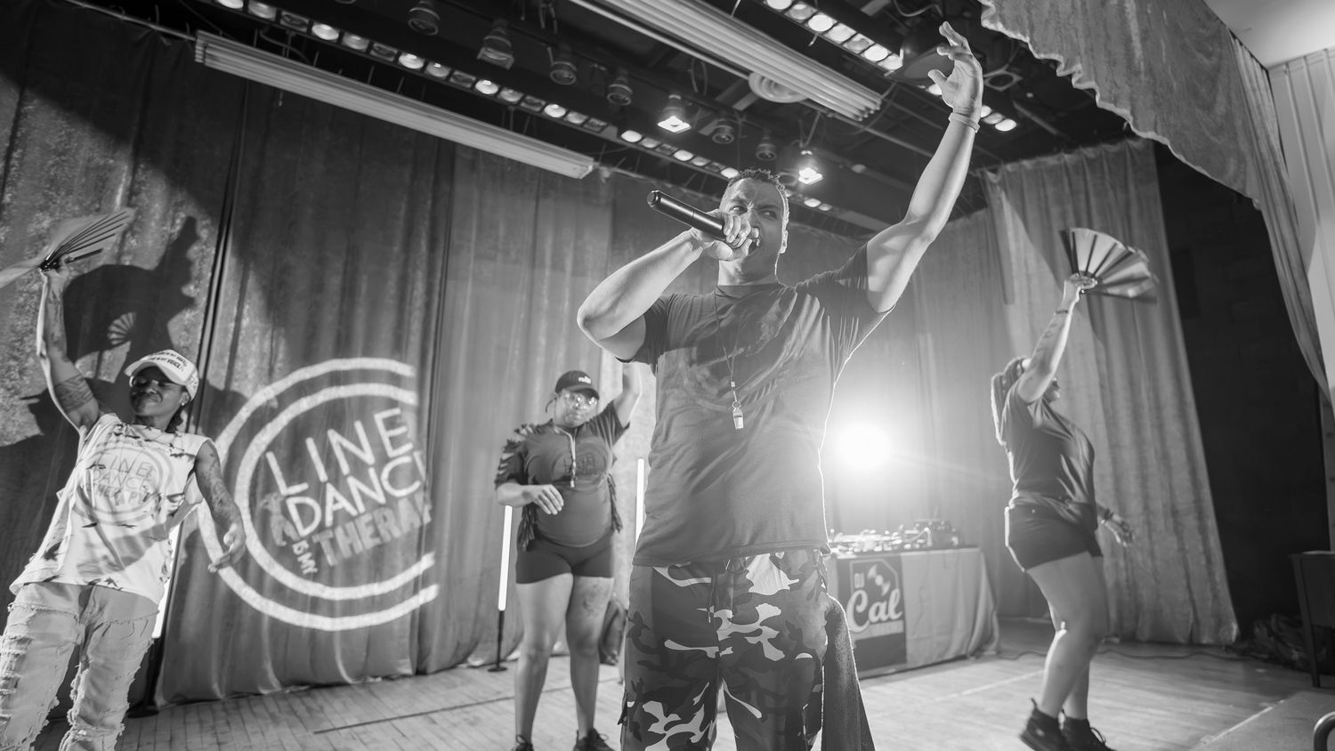 Black and white photo of energetic performer on stage at a line dance event.