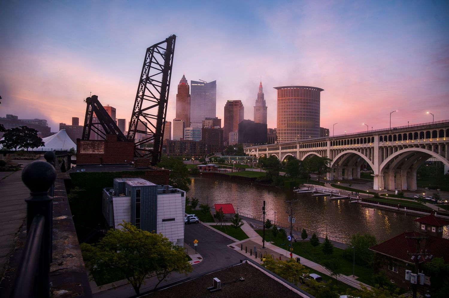 Cleveland skyline at sunset with river, historic bridge, and colorful sky.