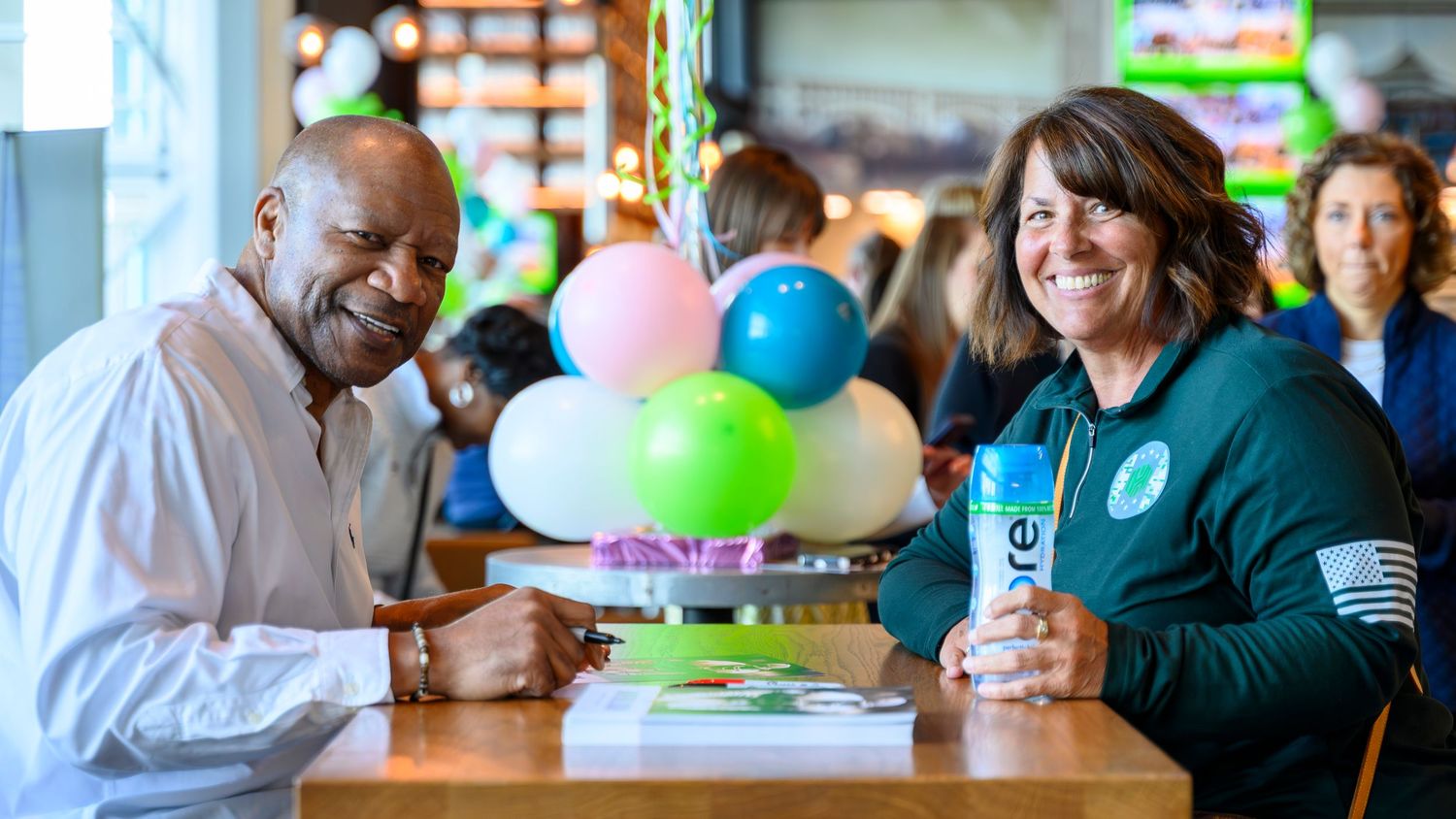 Man and woman smiling together at a table with balloons at a casual restaurant event.
