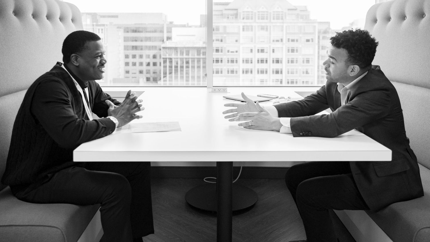 Two men in suits having a professional discussion at a white table in a modern office setting.