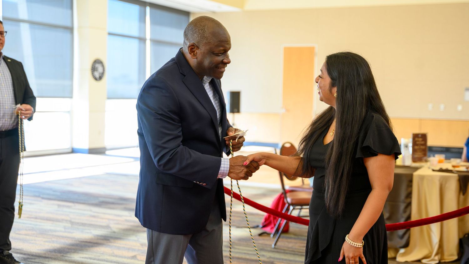 Professional man in blue suit shaking hands with woman at a formal networking event indoors.