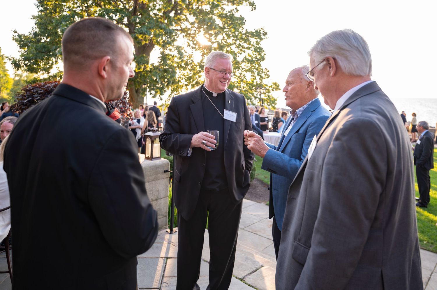Four men in formal attire engage in conversation outdoors at an evening reception event.