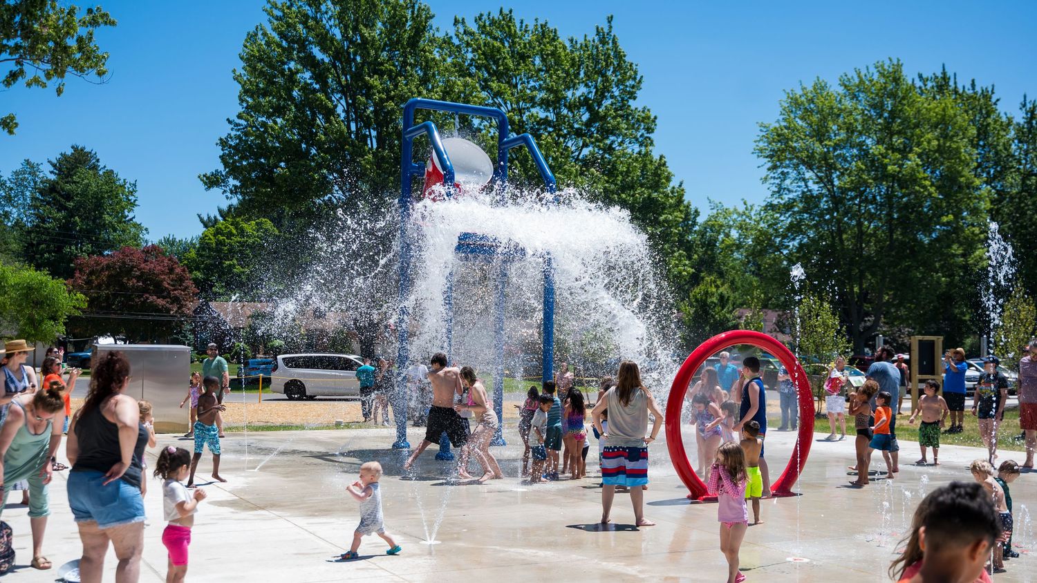 Children and families play at a colorful outdoor splash pad water park on a bright sunny summer day.