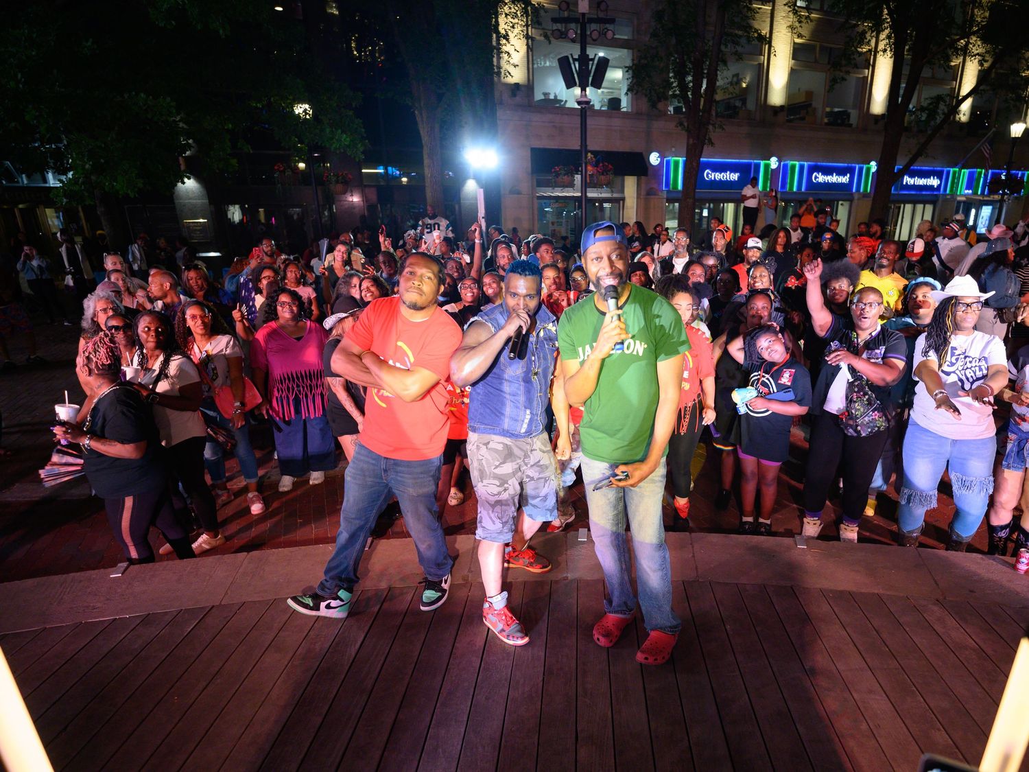 Two performers on an outdoor stage entertain a large crowd at a lively nighttime event in an urban plaza.
