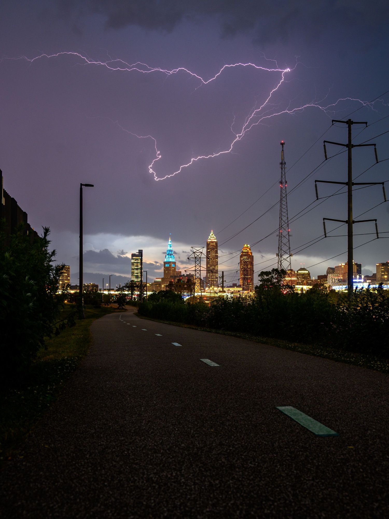 Lightning strikes over Atlanta city skyline at night with a dark road and power lines in the foreground.