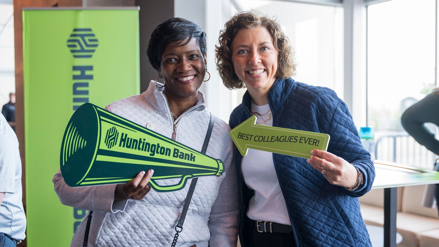 Two women smile holding Huntington Bank branded signs at a corporate appreciation event.