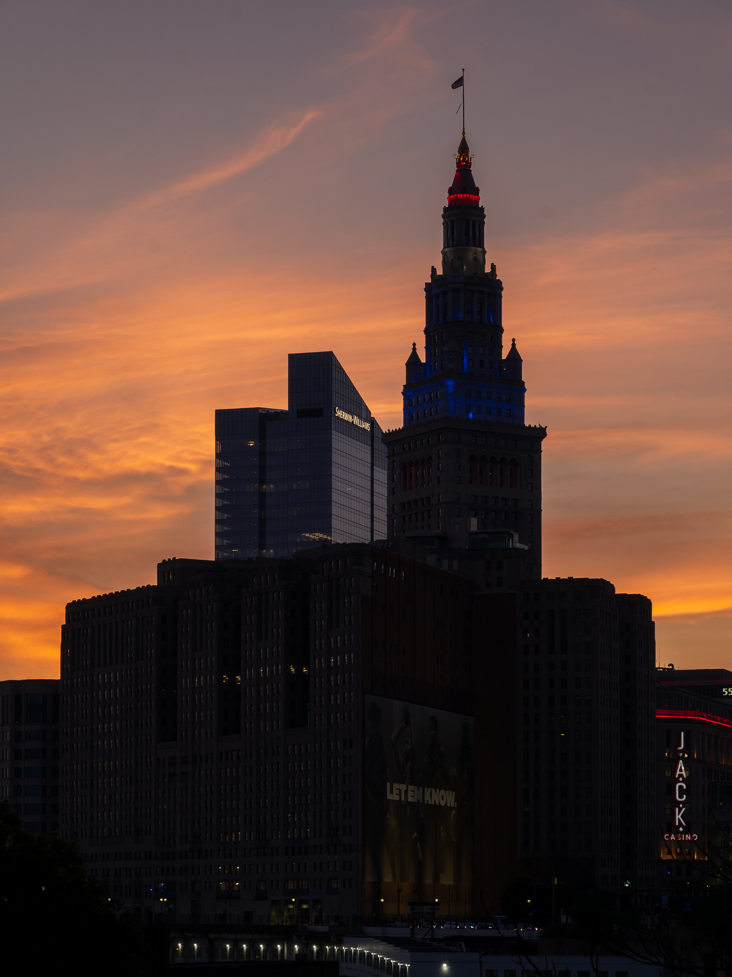 Cleveland skyline at sunset with Terminal Tower lit in red and blue against a vivid orange sky.