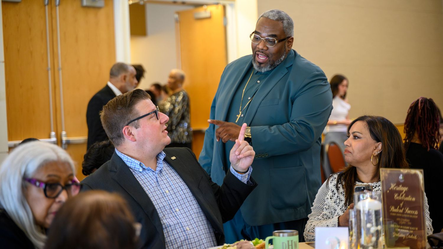 Three professionals engage in lively conversation at a formal networking dinner event in a conference room.
