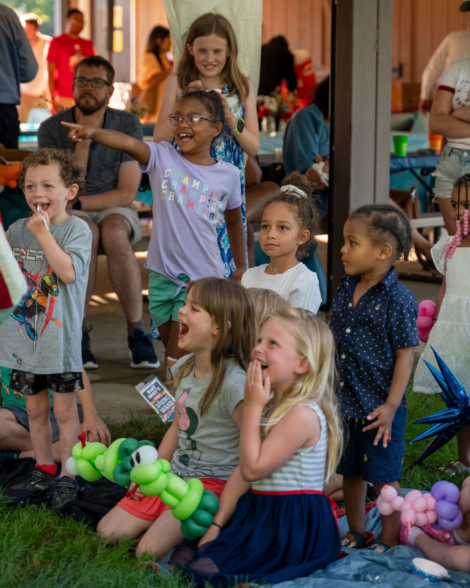 Diverse group of excited children watching a show with balloon animals at outdoor event.