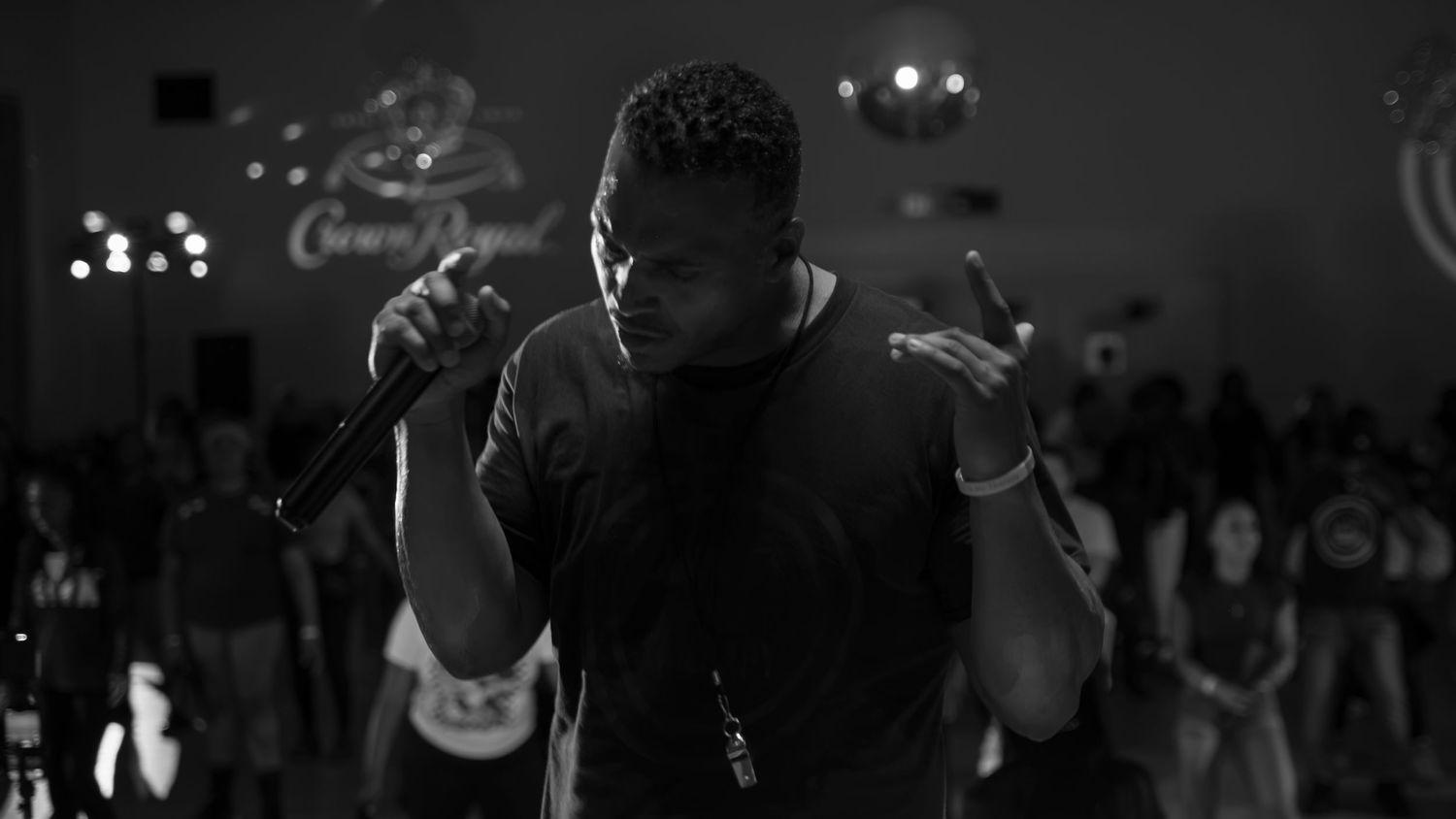 Black and white photo of a male rapper performing on stage holding a microphone in a dimly lit venue.