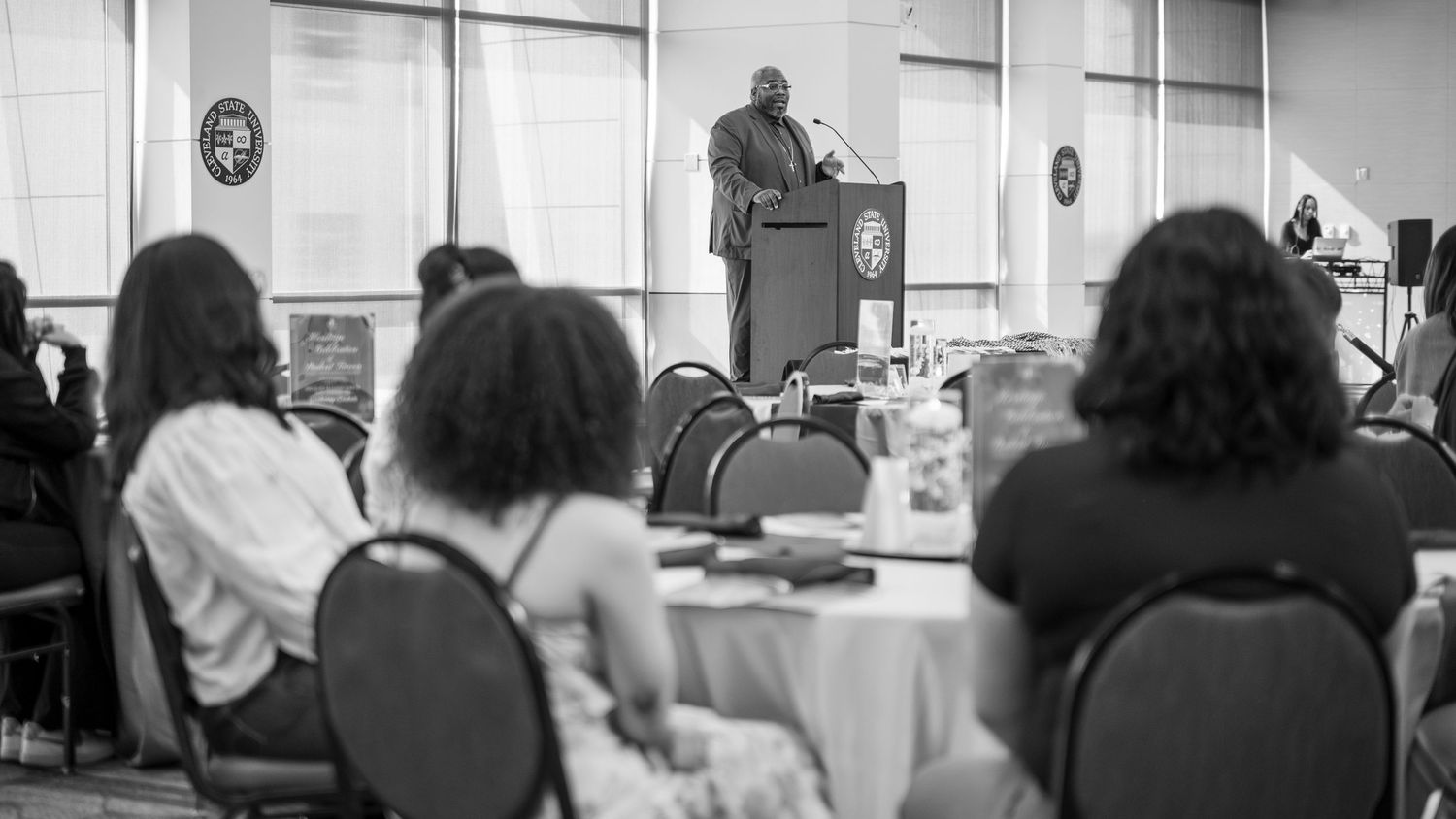 Black and white photo of a speaker addressing an audience at a formal banquet or conference event.