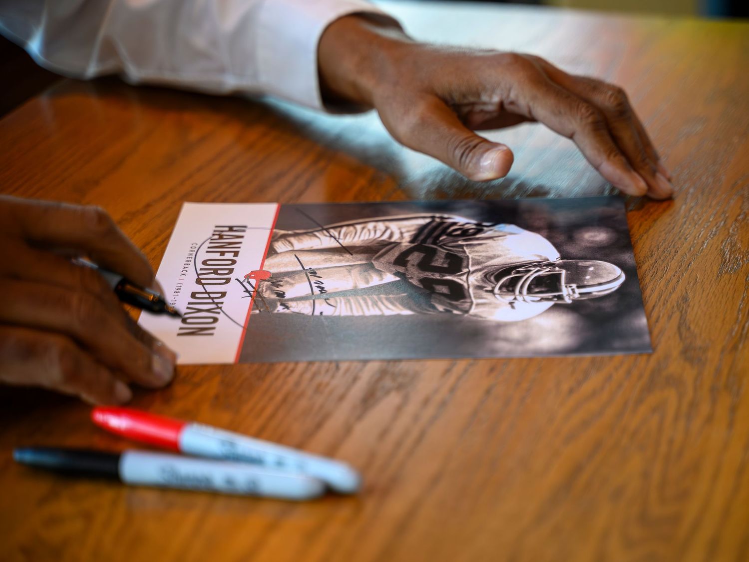 Close-up of hands signing an autograph on a black and white photo card with markers.