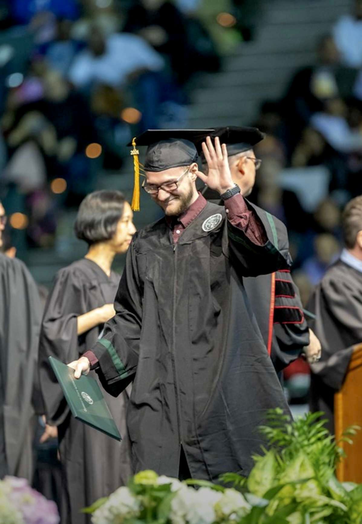Graduate in cap and gown waving during Cleveland State University commencement ceremony.