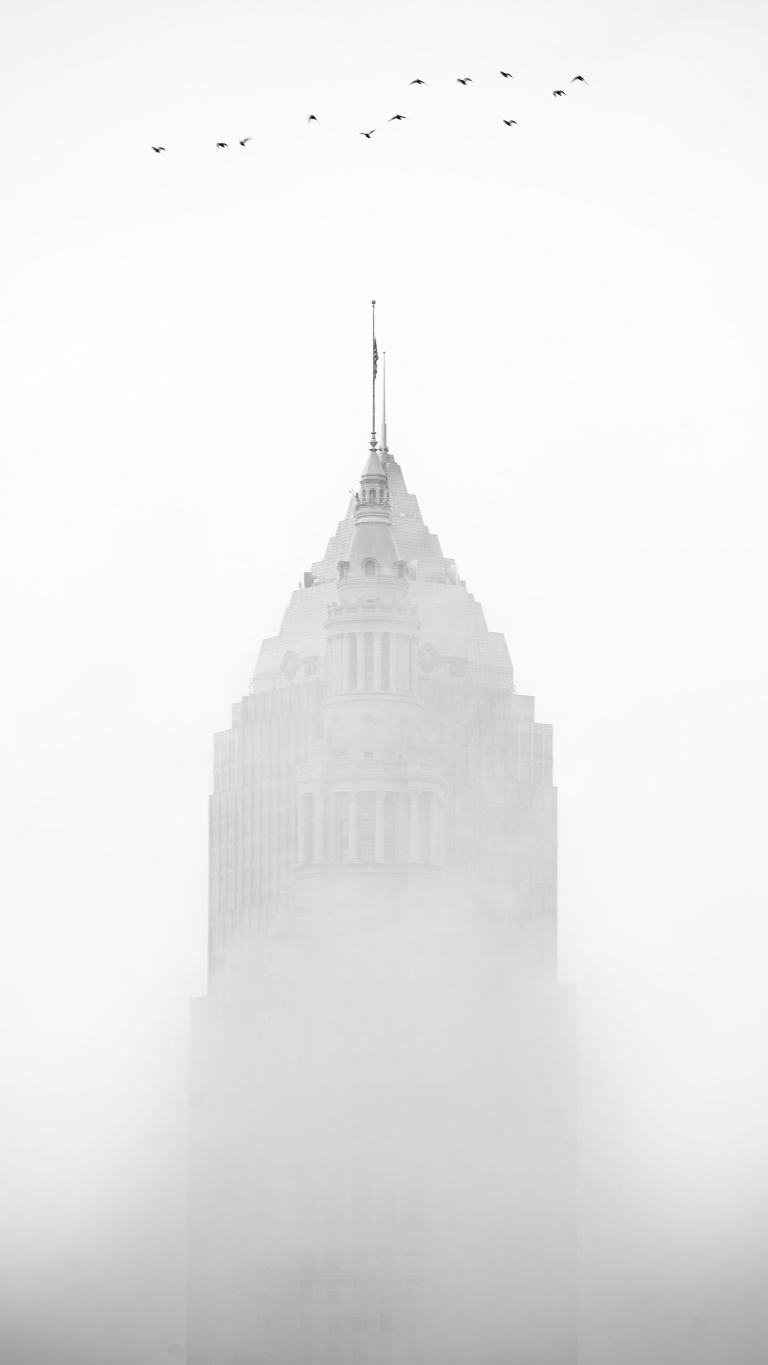 Empire State Building emerging from dense fog in a dramatic black and white cityscape photo.