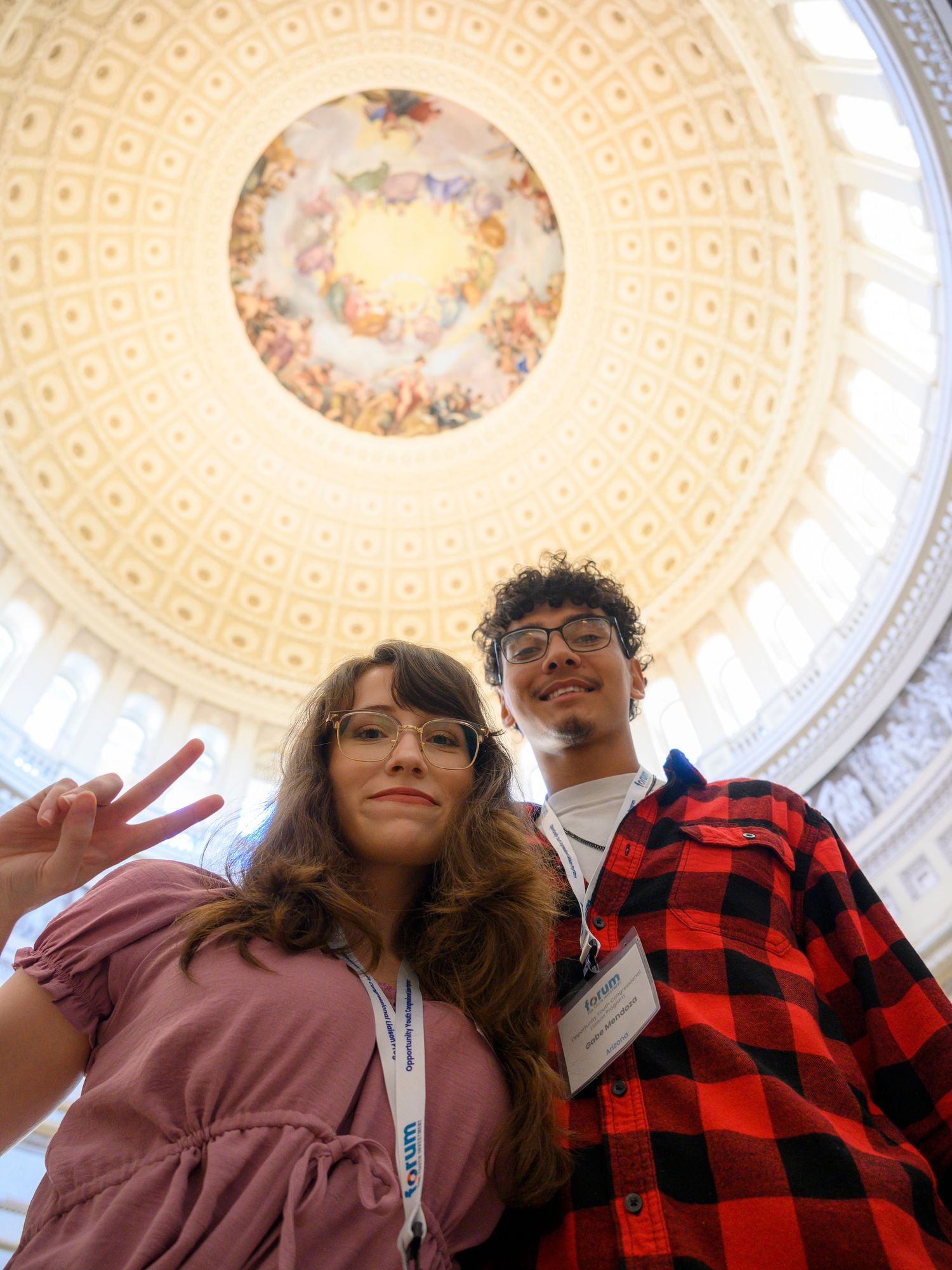 Two young people pose for a selfie inside the U.S. Capitol Rotunda beneath its ornate painted dome.