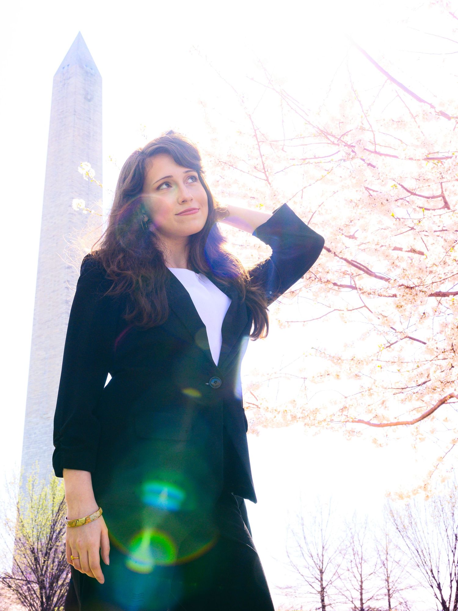 Young woman in black blazer posing near the Washington Monument surrounded by cherry blossoms.