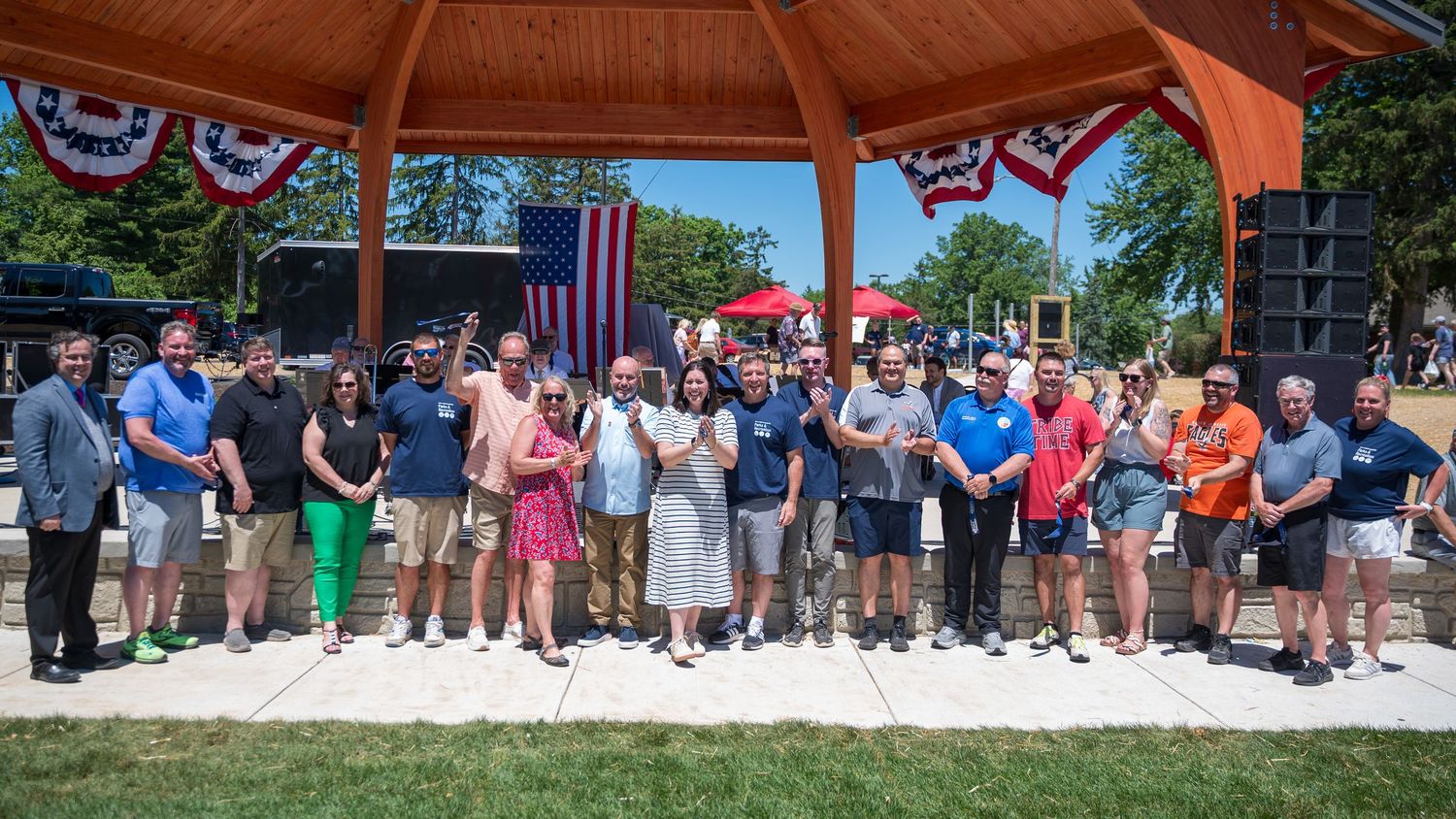 Large group of people posing outdoors near a gazebo decorated with American flags at a community event.