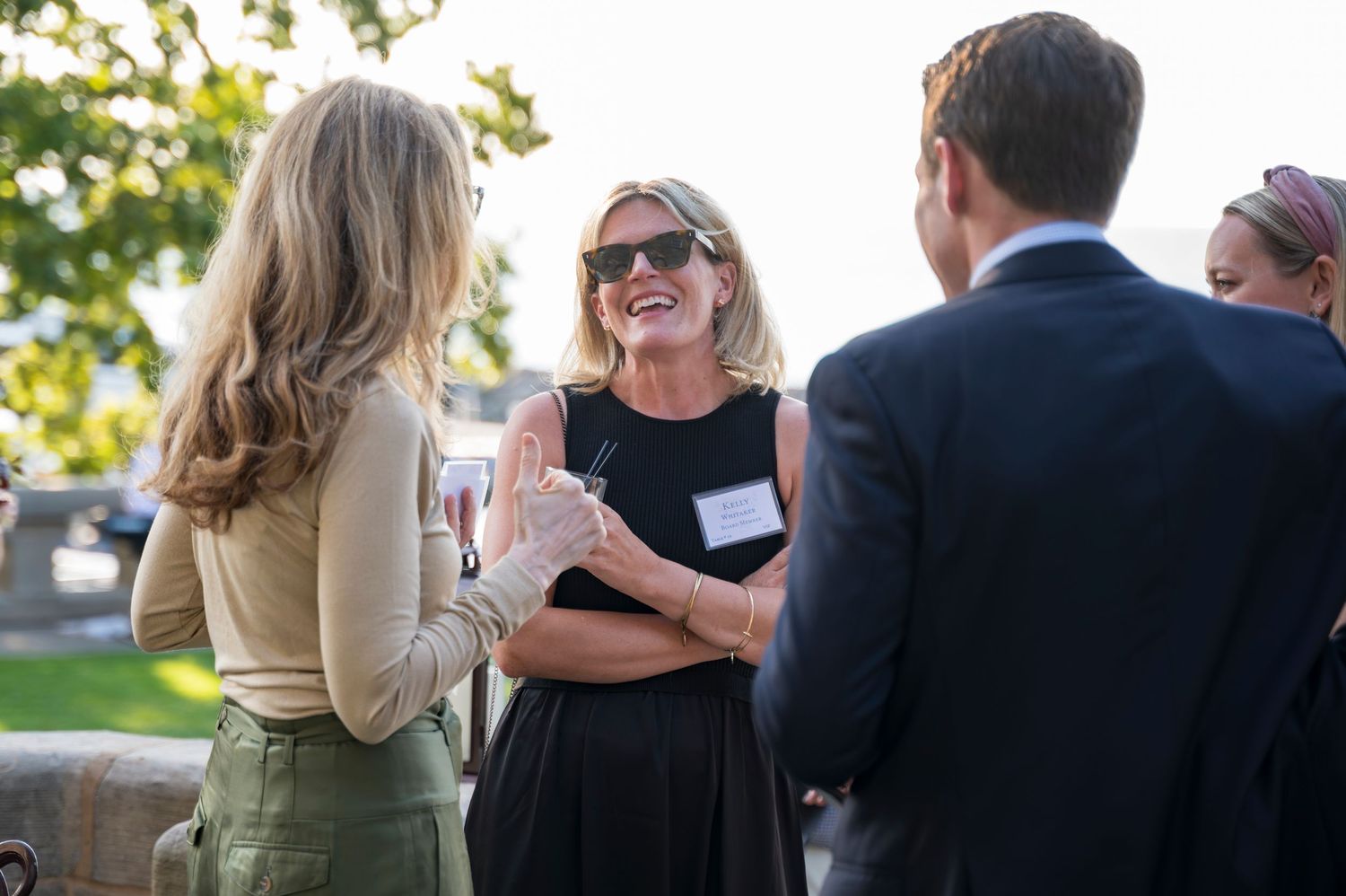Three adults laughing and socializing at an outdoor networking event during golden hour.