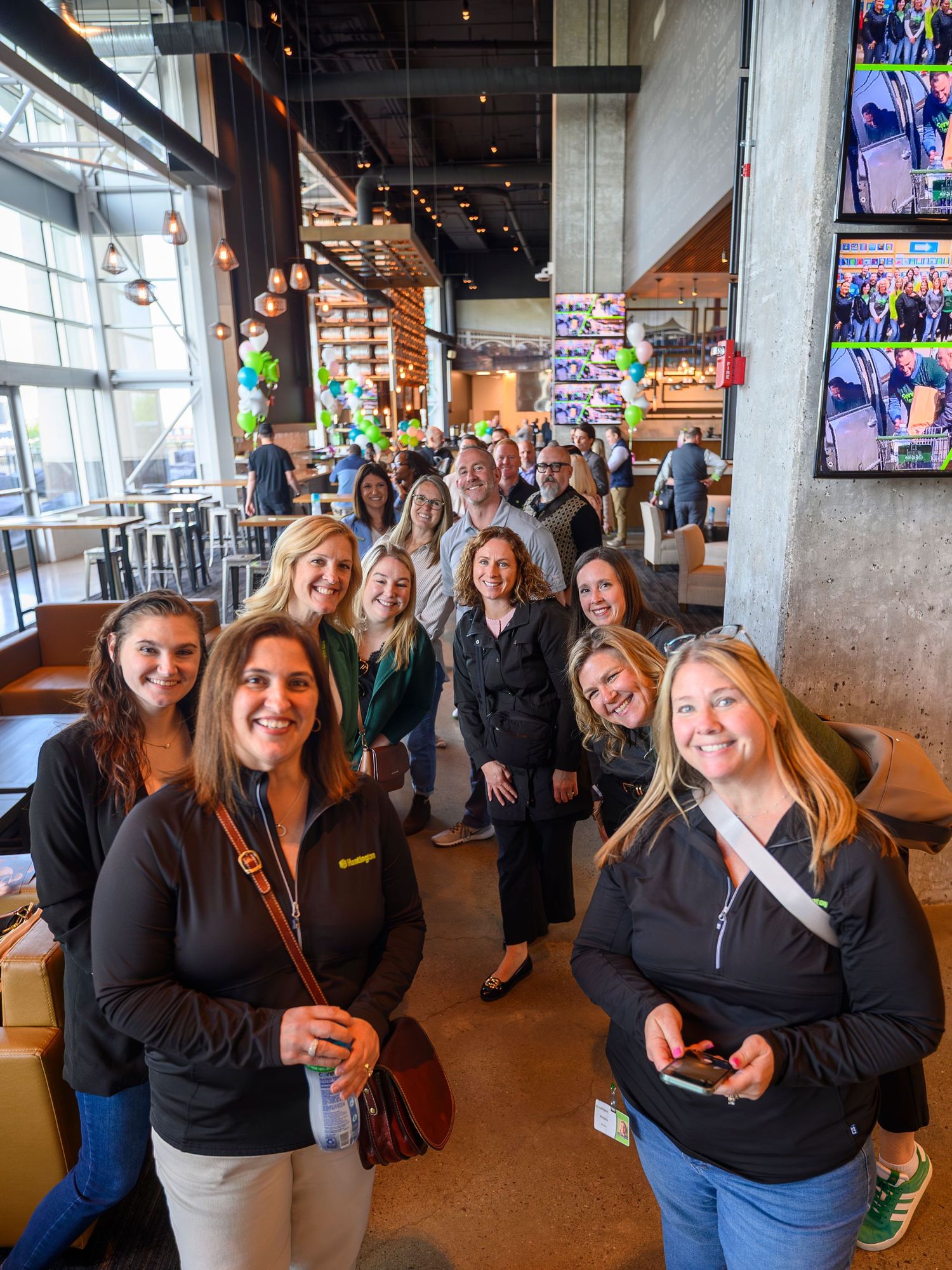 Group of smiling professionals posing together inside a modern restaurant or brewery.