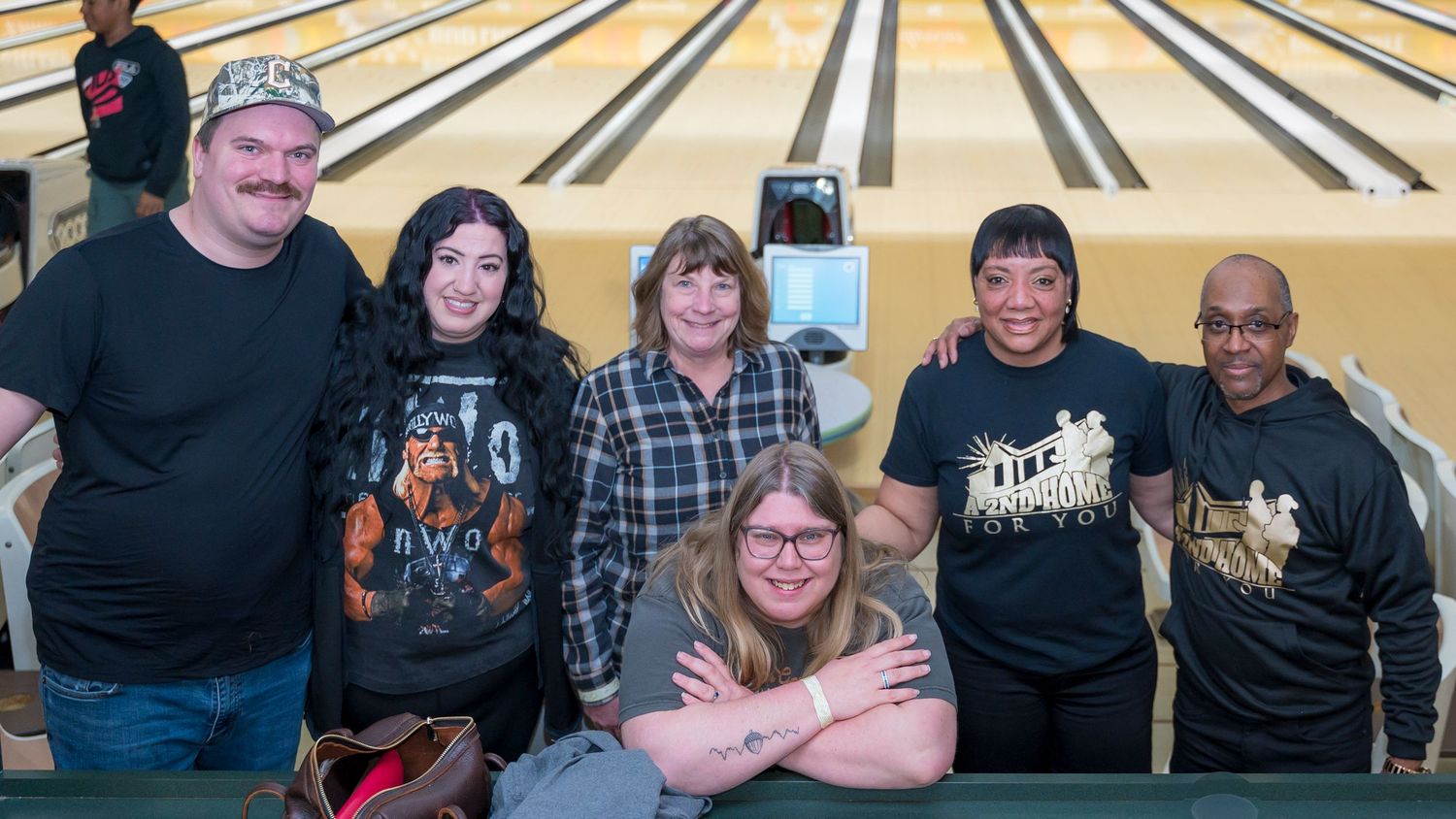 Group of six friends pose together smiling at a bowling alley lane.
