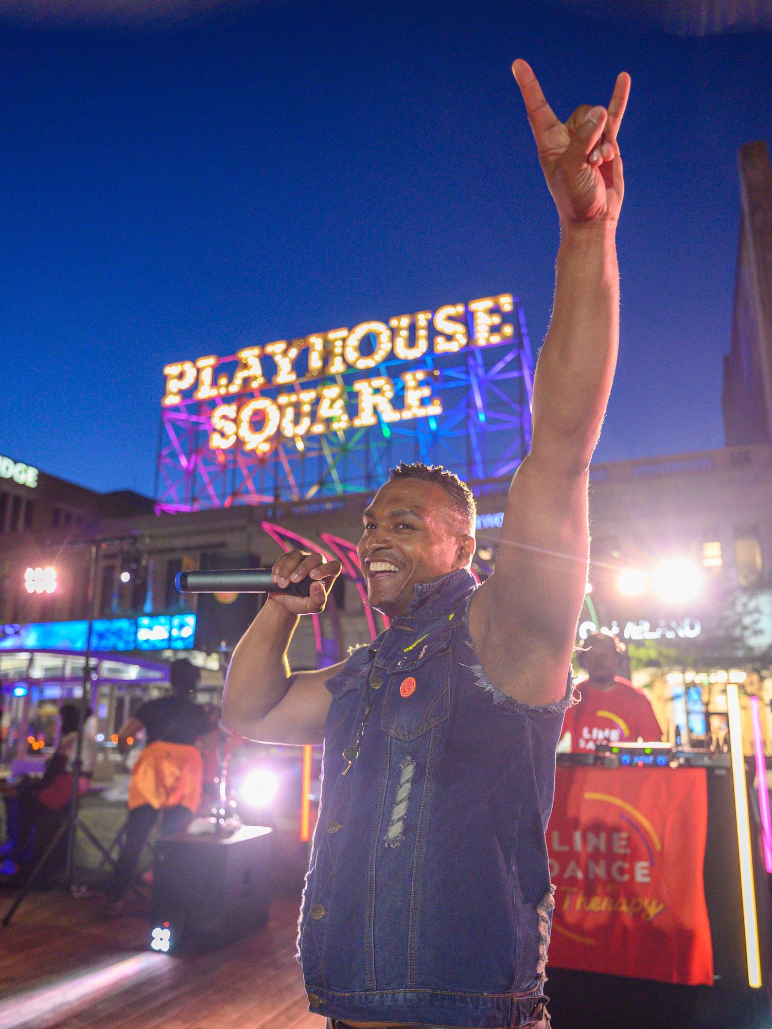 A performer sings on stage at Playhouse Square in Cleveland, raising a rock hand gesture under vibrant neon lights at night.