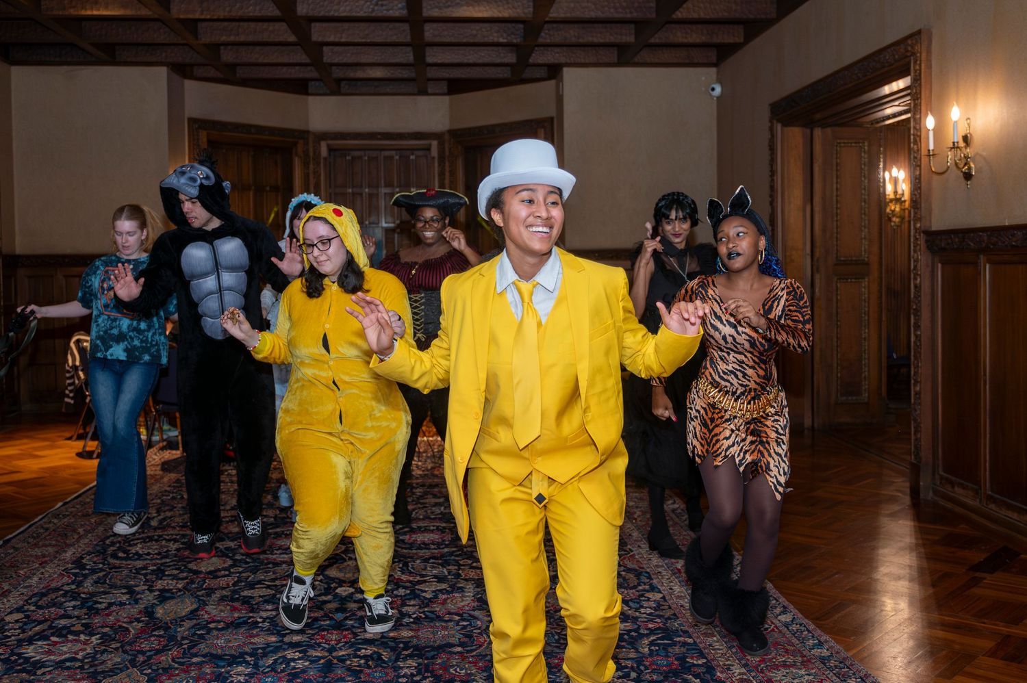 Group of people in colorful Halloween costumes dancing in an elegant wood-paneled ballroom.