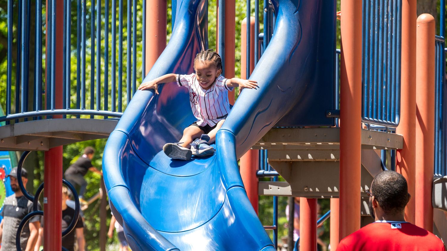 Child sliding down blue playground slide at outdoor play structure on sunny day.