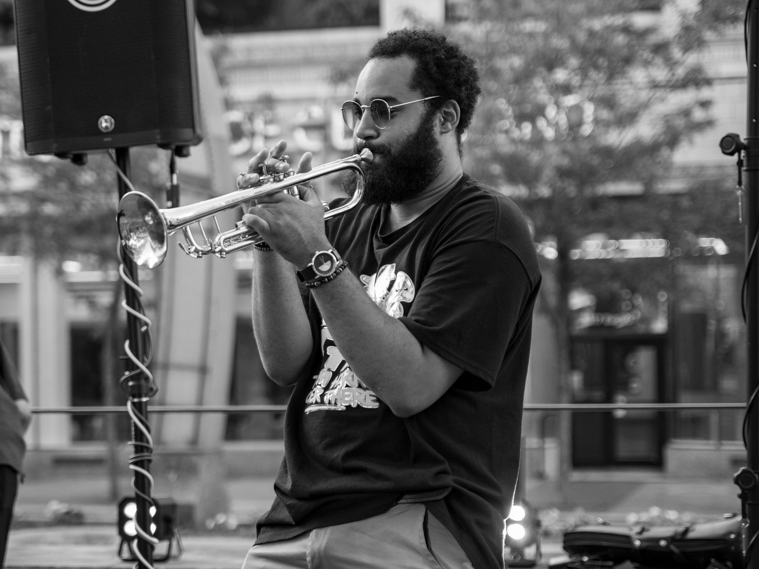 Black and white photo of a bearded man playing trumpet outdoors at a live music event.
