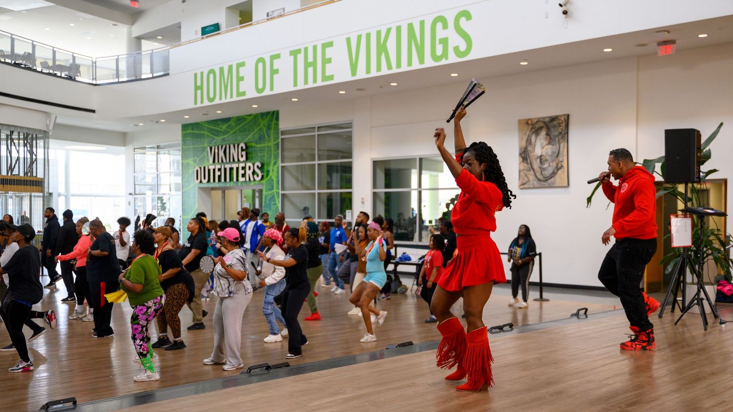Performers in red outfits dance before a crowd inside a Home of the Vikings branded venue.