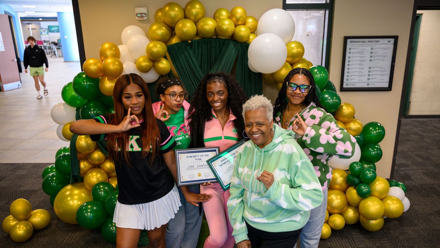 Group of women celebrating with green and gold balloons, holding certificates at a school award ceremony.