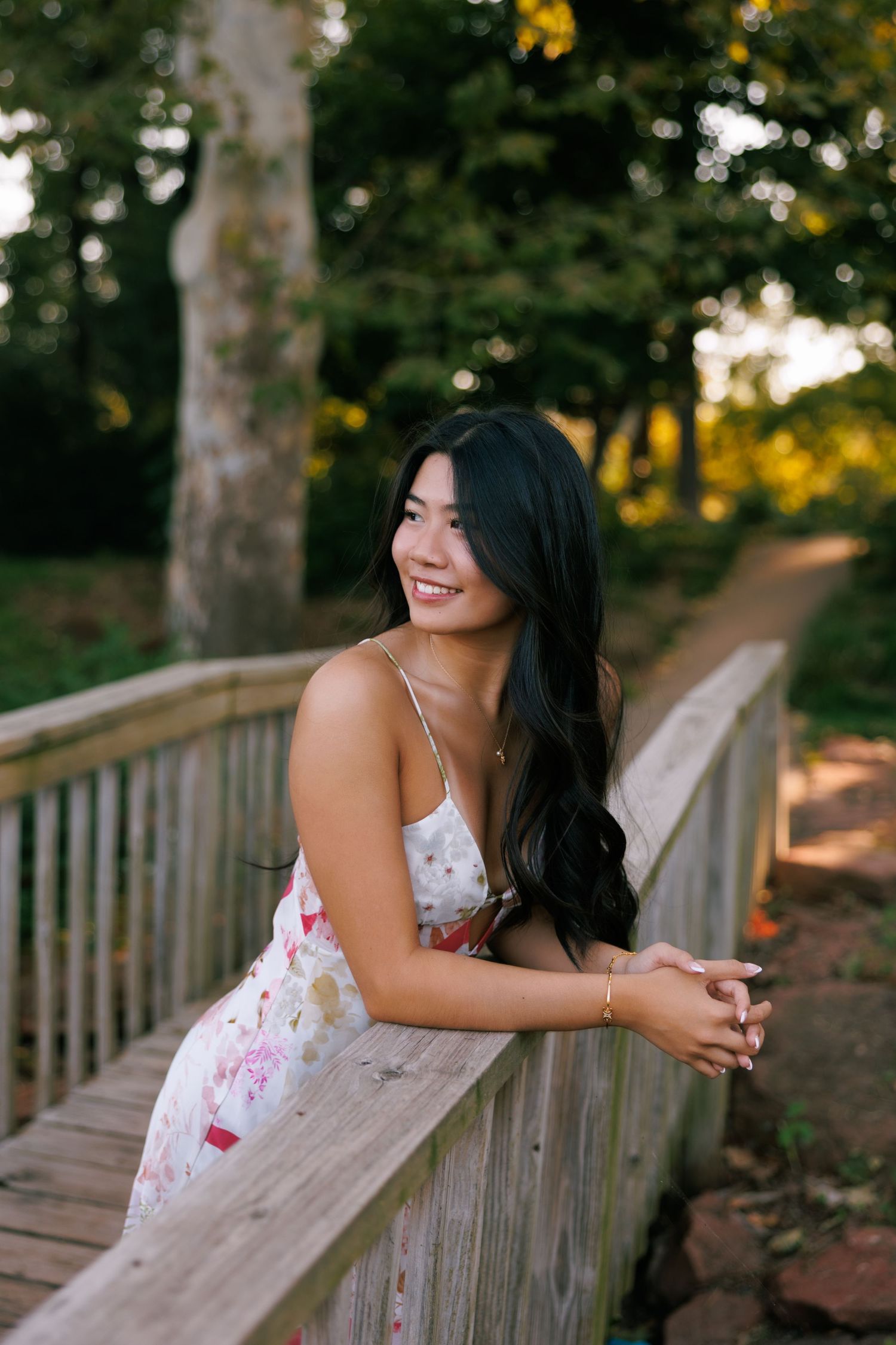 A floral white dress creates a romantic scene on a wooden bridge surrounded by trees.