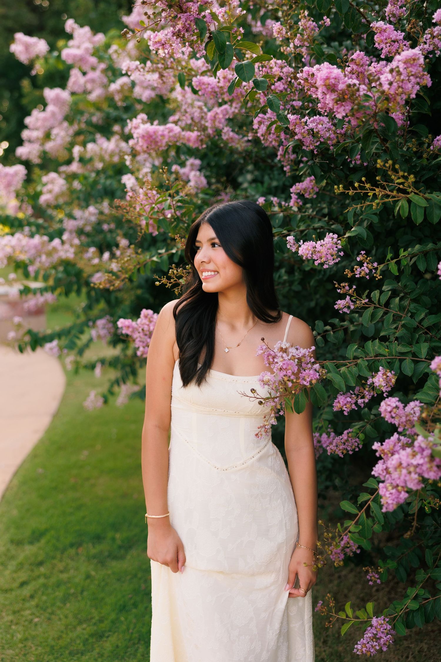 A cream dress complements blooming pink flowers in a lush garden setting.