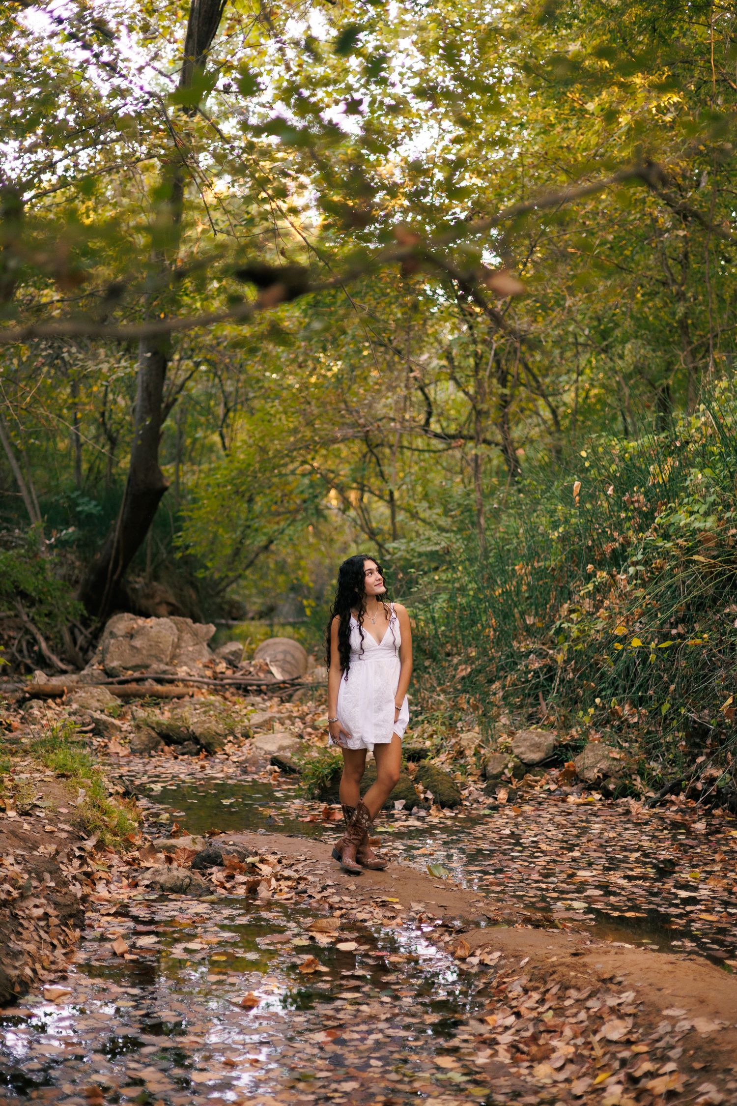 Autumn photography session along a leaf-covered creek bed surrounded by golden trees.