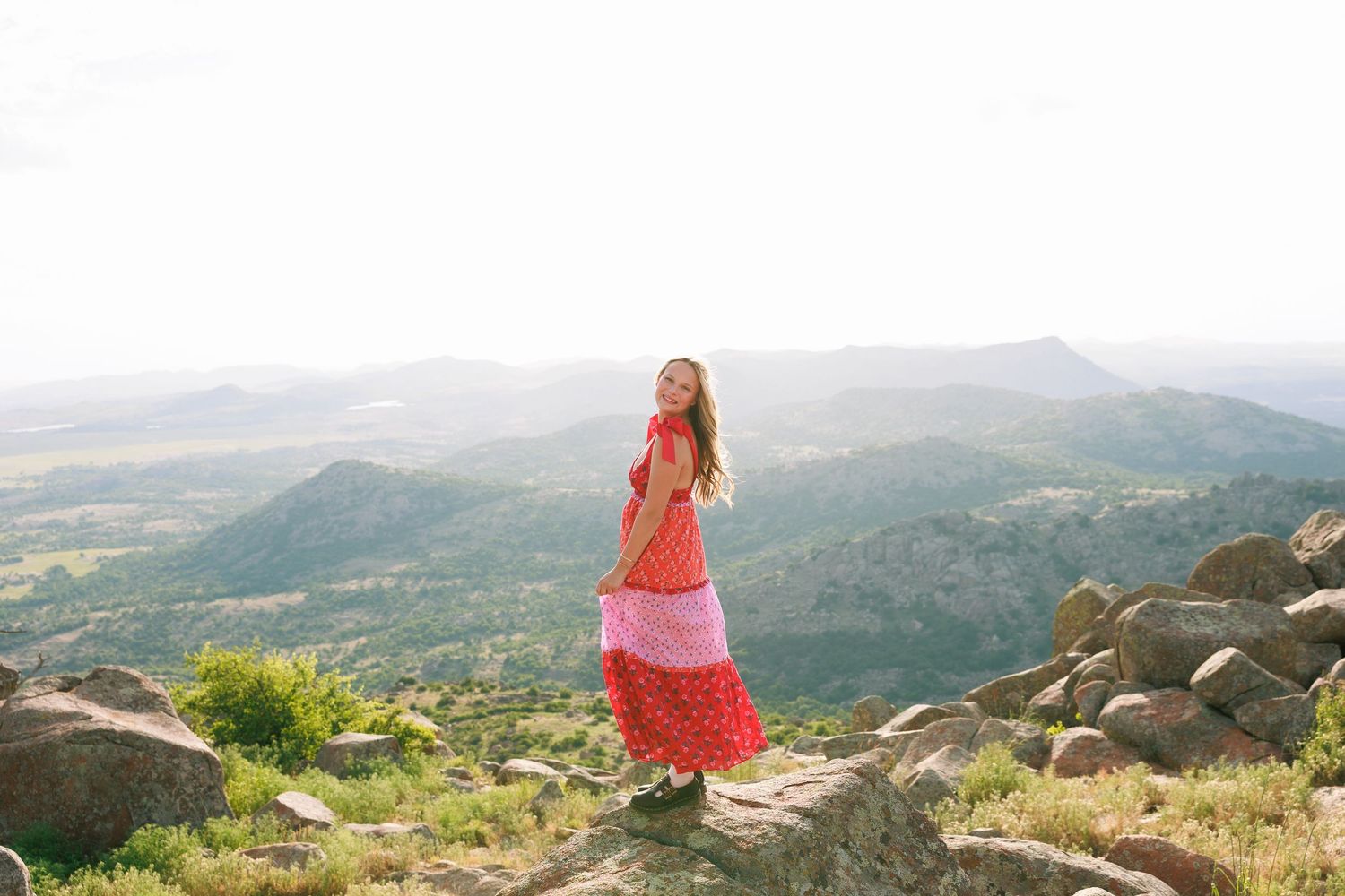A flowing red dress stands out against a mountainous landscape at sunset.
