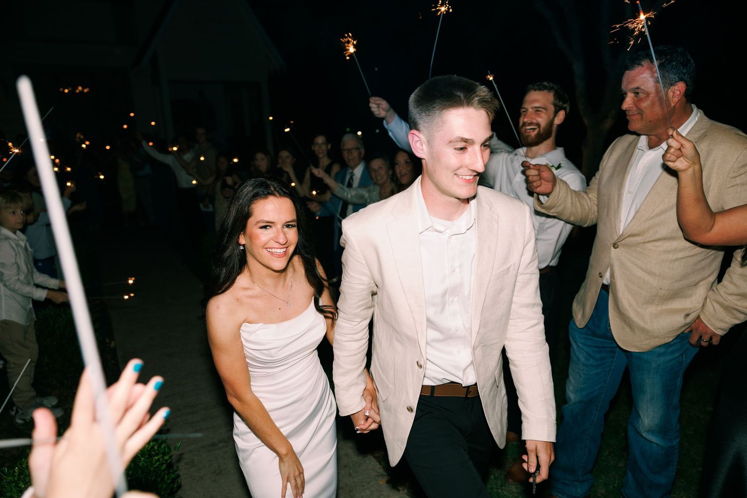 Wedding reception party guests dancing and celebrating at night under sparklers.