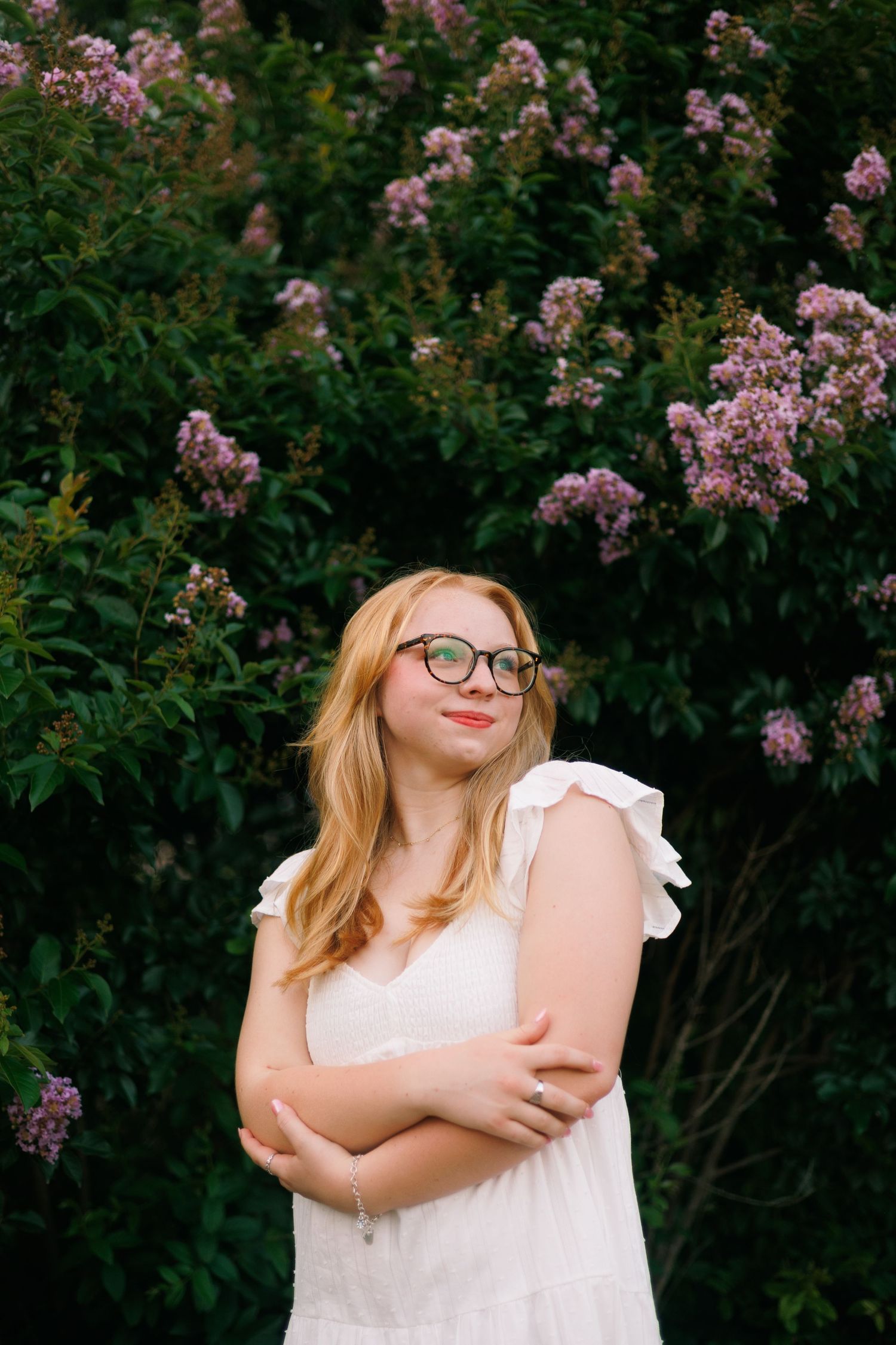 A white dress stands out against pink flowering bushes in a lush garden setting.