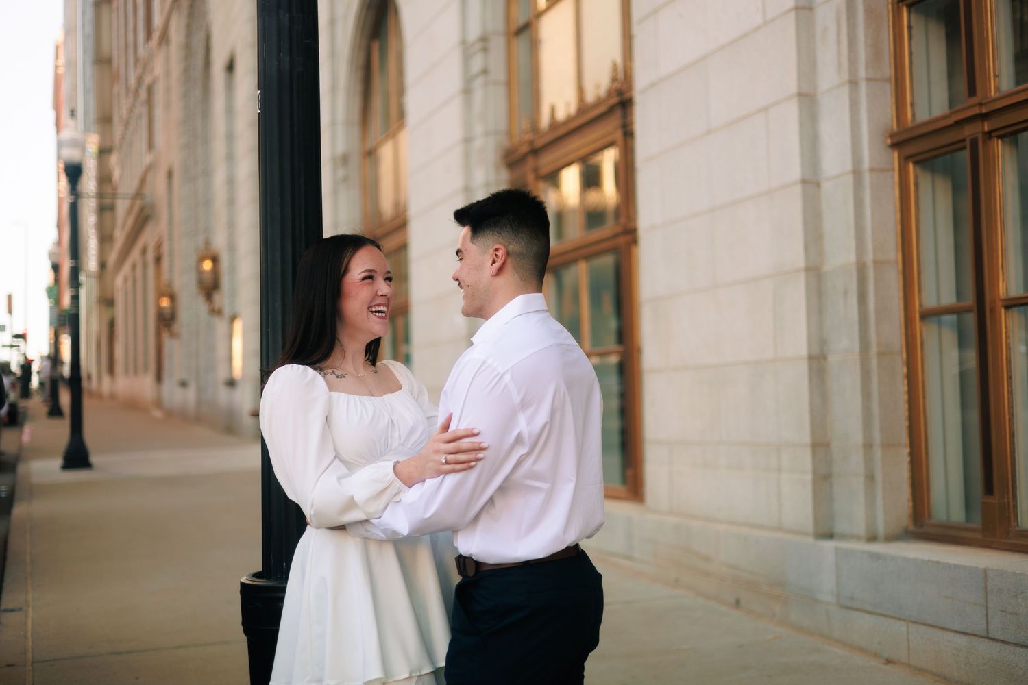 A couple embraces in an elegant indoor setting with white stone columns and natural lighting.