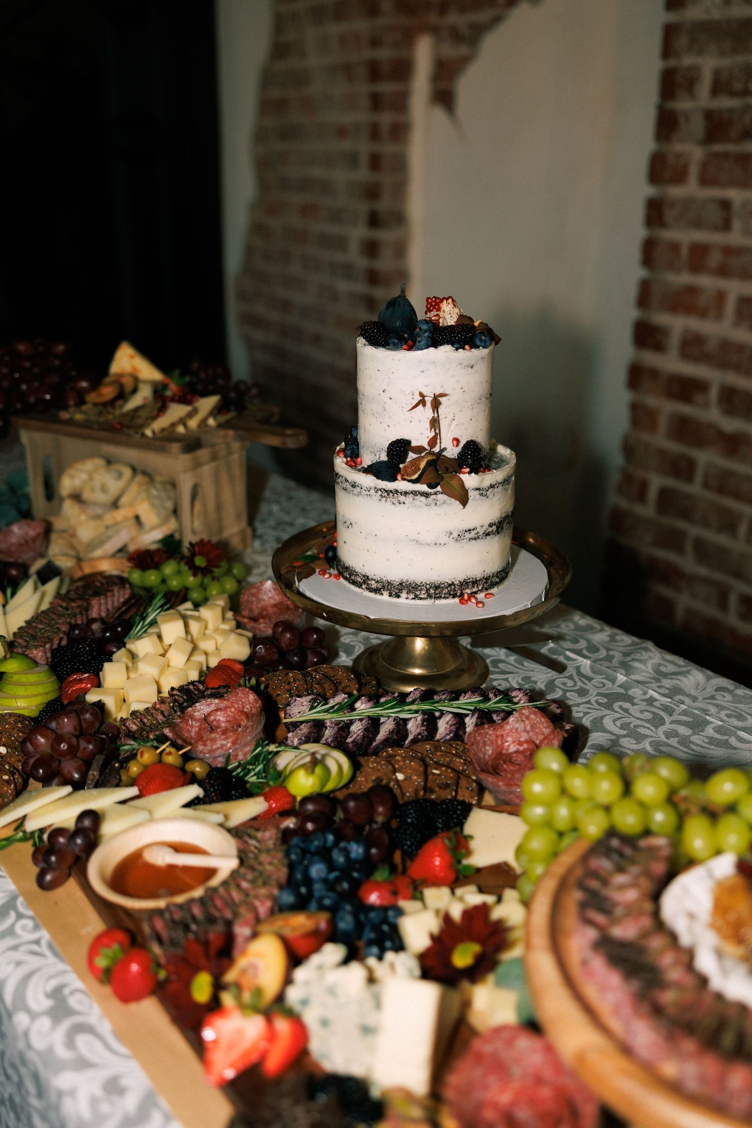 Wedding reception dessert table with a white cake and charcuterie board featuring fruits and cheeses.