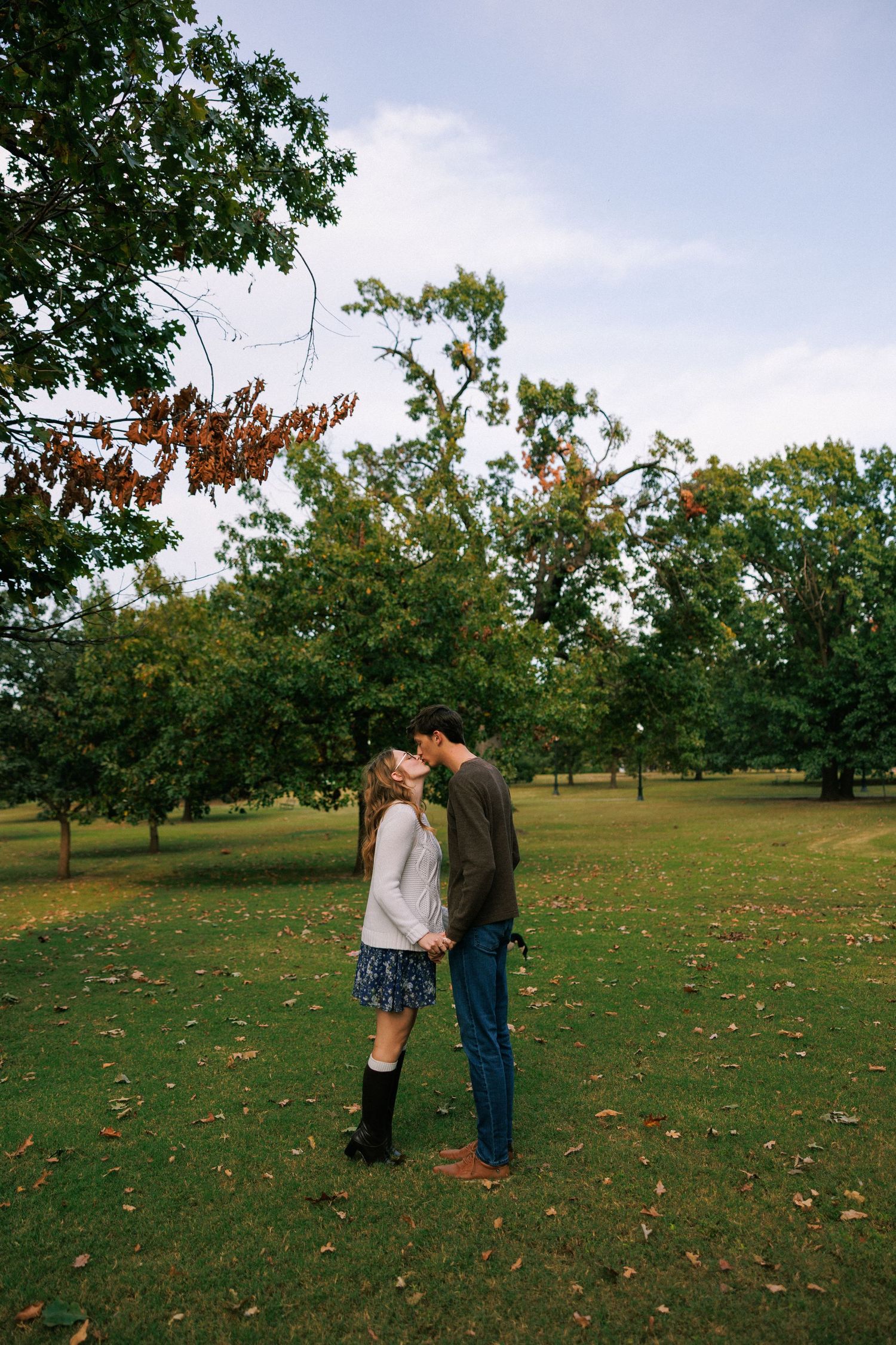 Couple sharing romantic moments in a grassy park setting during autumn.