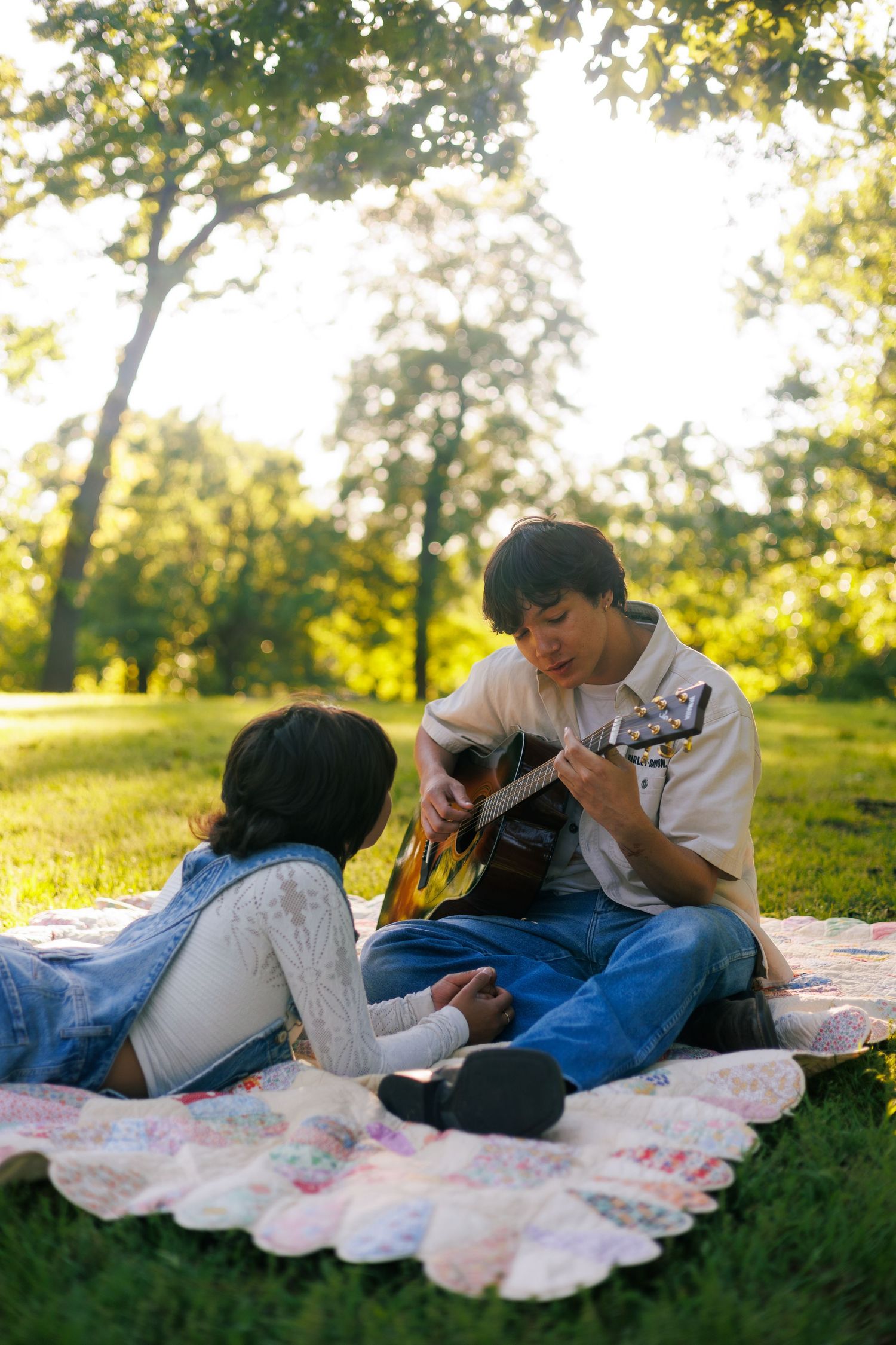 Couple relaxing on a blanket in the grass while playing guitar during golden hour.