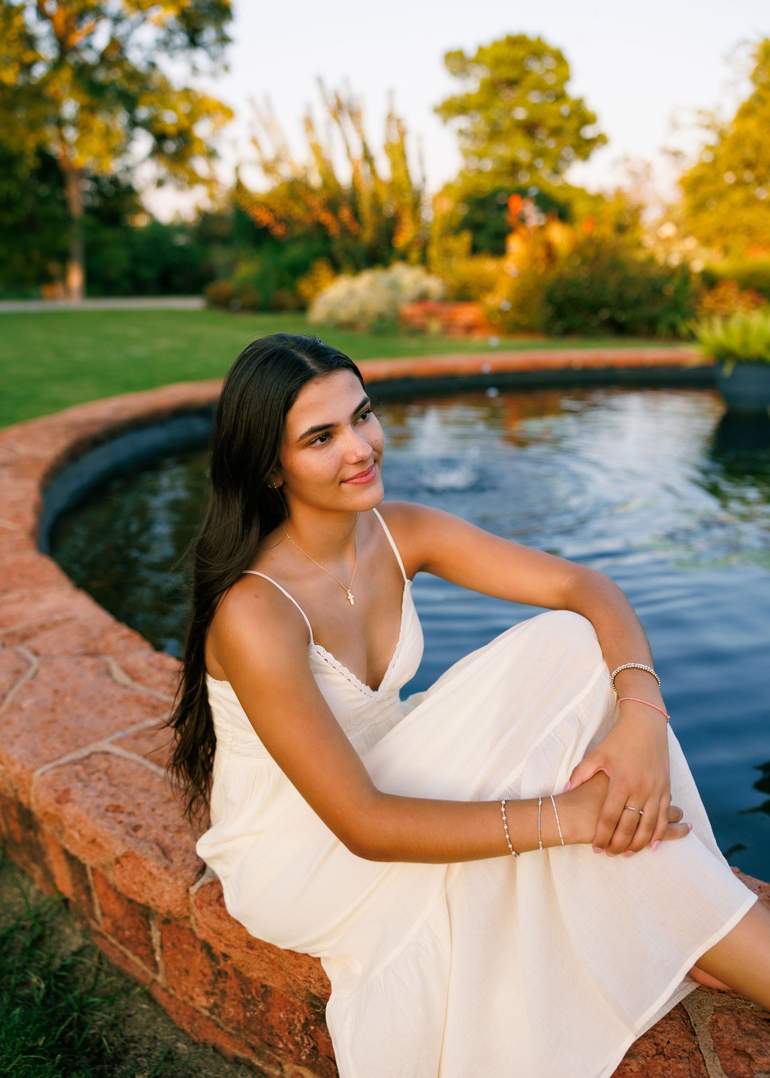 Elegant white dress portraits by a stone-edged reflecting pool at golden hour.