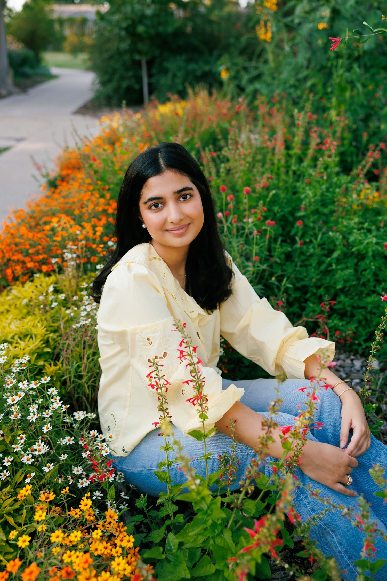 A sunny garden photoshoot featuring yellow flowers and someone wearing a light yellow blouse and jeans.
