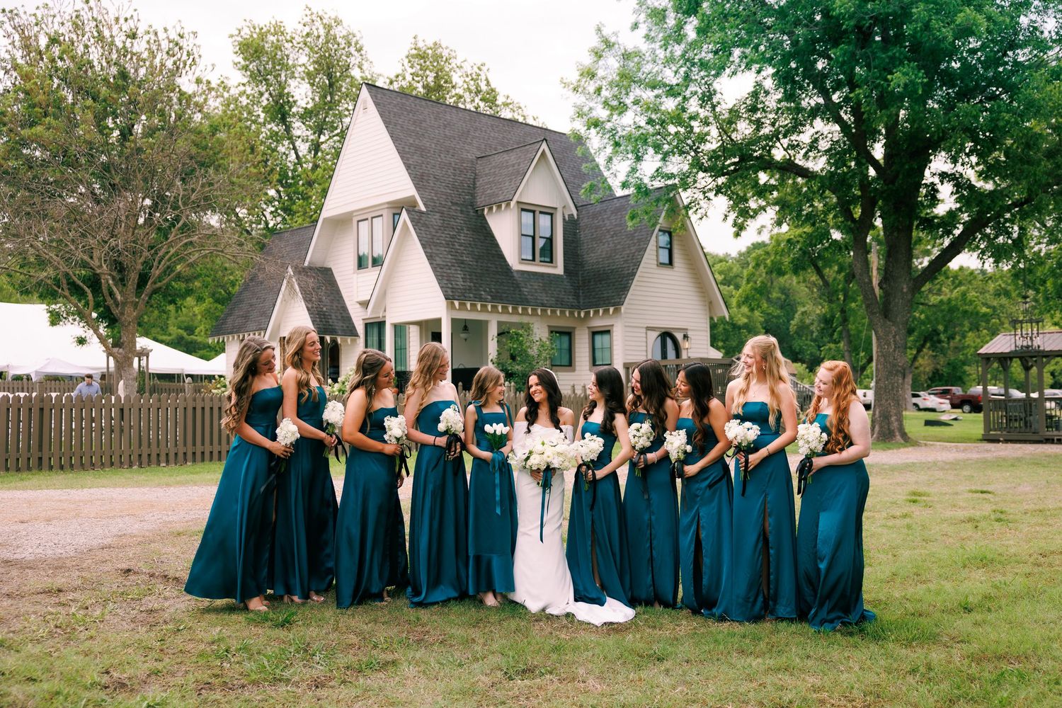 Wedding party in teal dresses posed on lawn in front of country house.