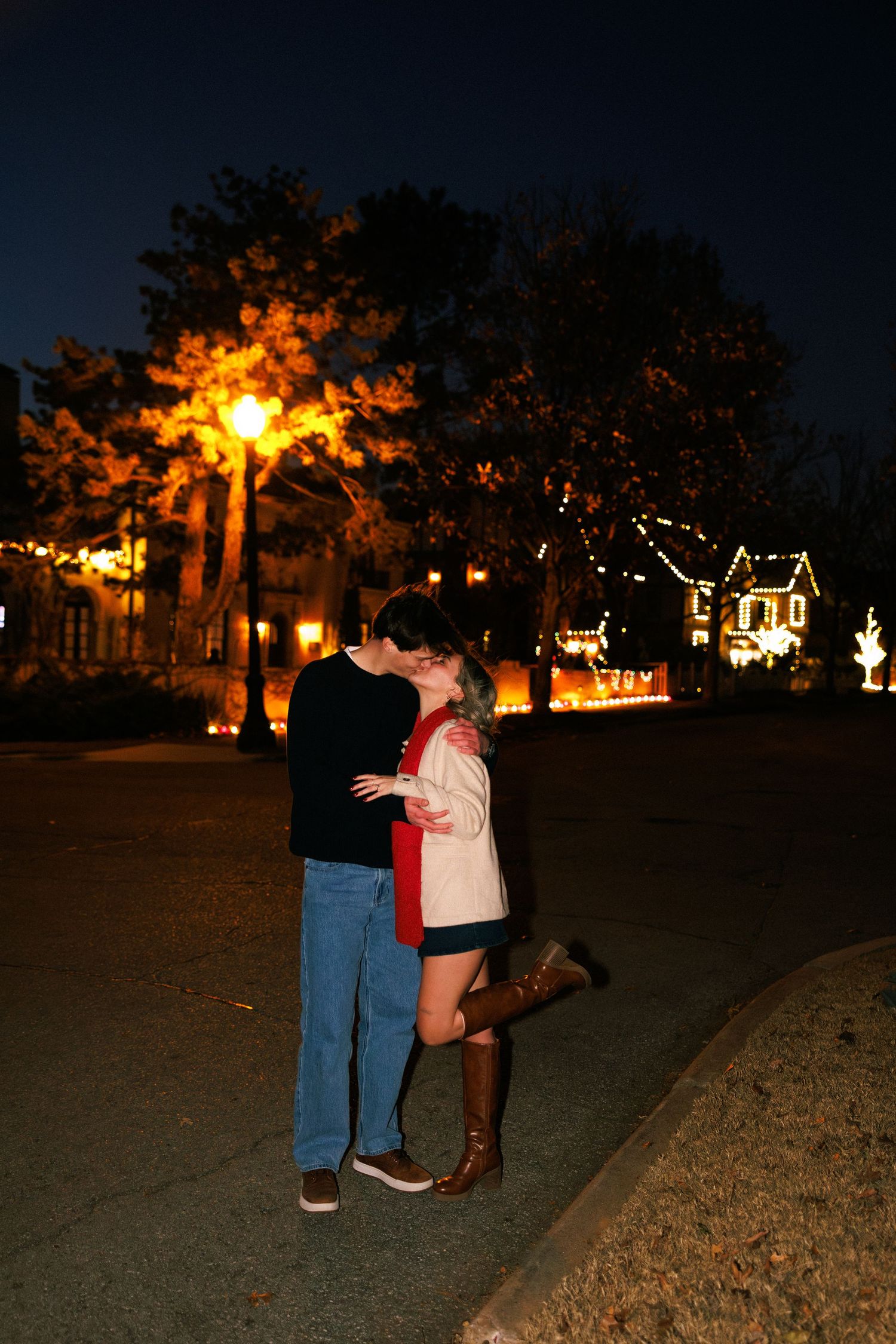 A couple embraces in a romantic nighttime setting with glowing lights in the background.