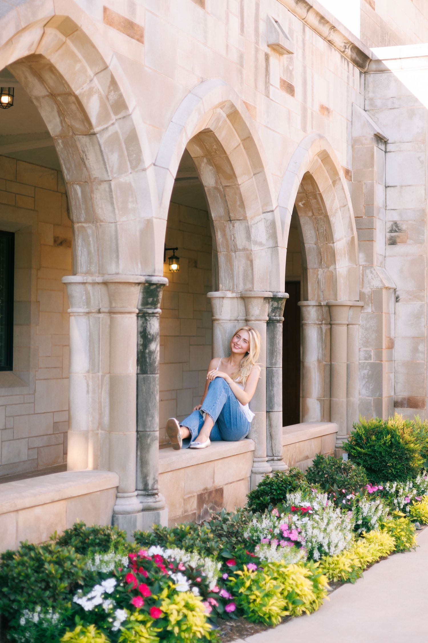Stone archway colonnade with colorful flower gardens and classical architecture.