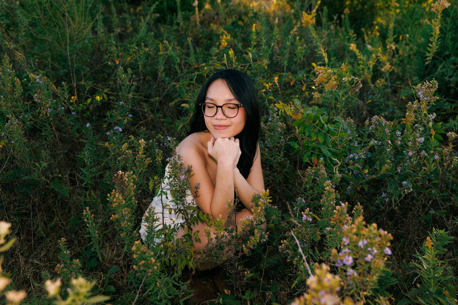 Person in casual attire poses among tall yellow wildflowers at golden hour.