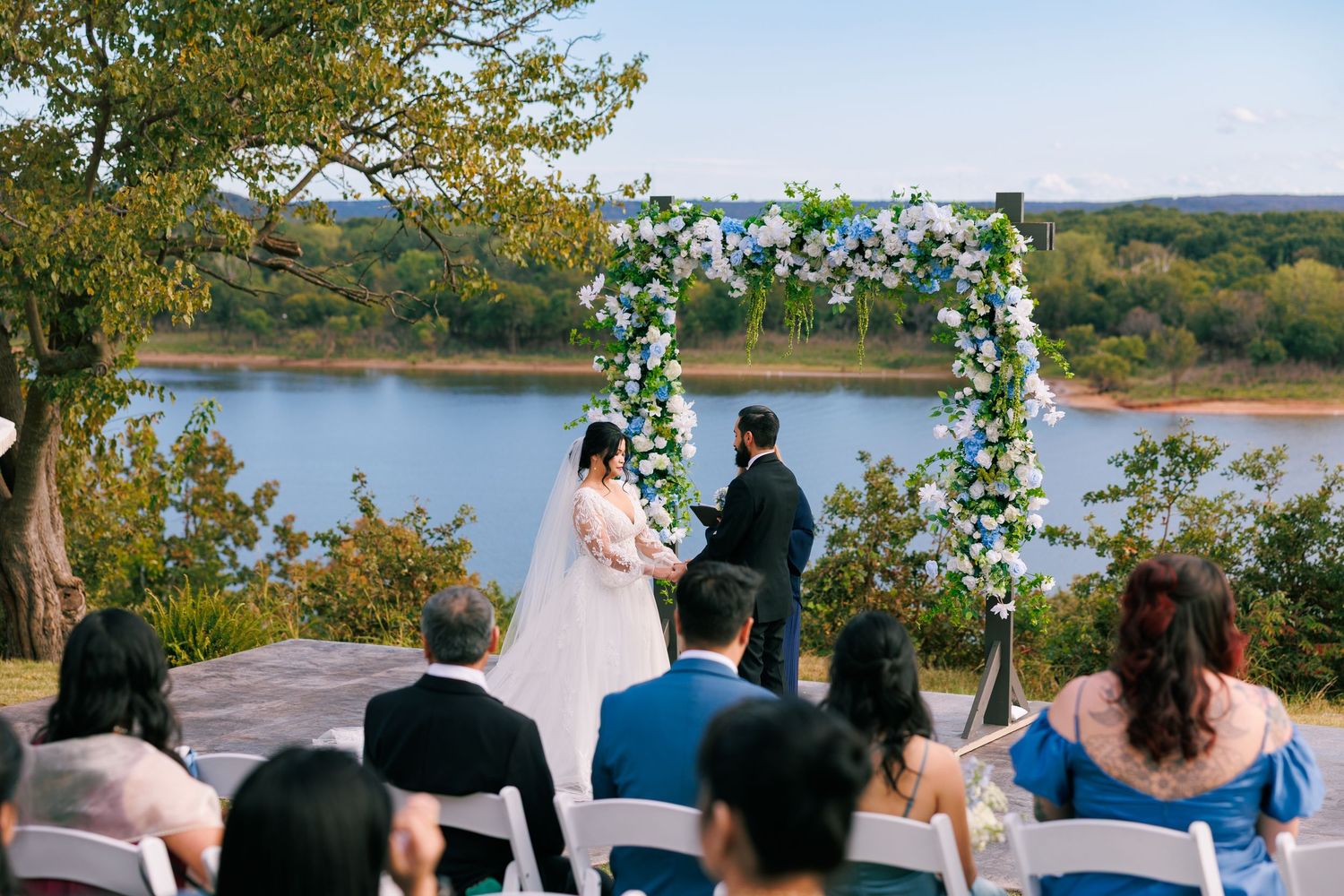 Outdoor wedding ceremony overlooking a serene lake with floral arch and seated guests.