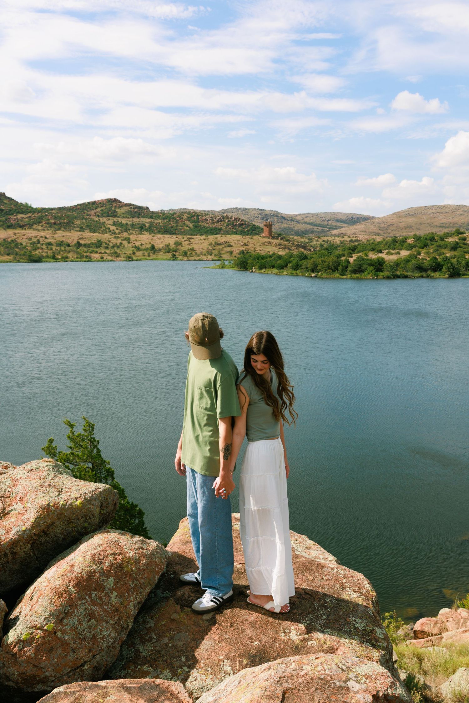 Two figures stand together on rocky outcrop overlooking a serene mountain lake.