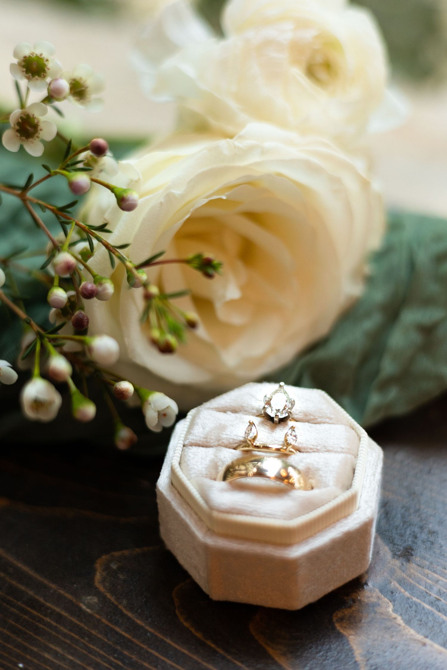 Wedding rings displayed in a white holder with delicate white roses in the background.