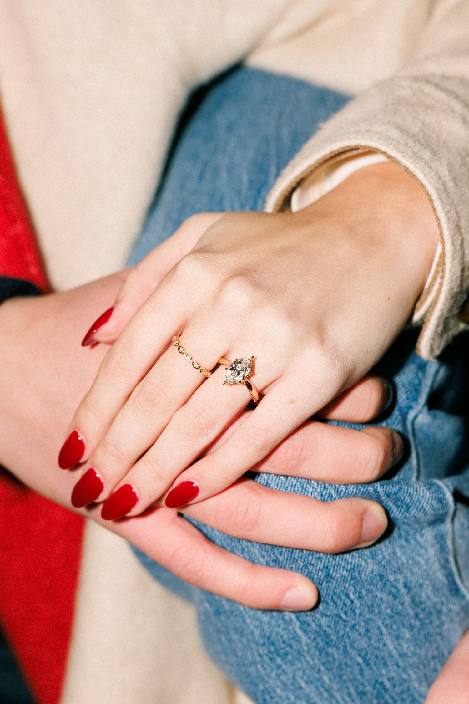 Hand wearing red nail polish and an engagement ring resting on denim.